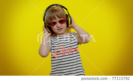 Funny playful blonde child kid listening music via headphones dancing disco fooling having fun party 77115792