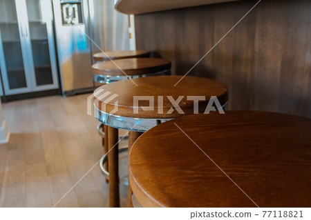 Row of retro wooden stools in front of wooden counter inside a modern style kitchen. Row of retro wooden stools in front of wooden counter inside a modern style kitchen. 77118821