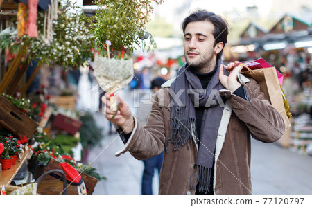 Smiling man in Christmas hat choosing flowers and decorations Smiling man in Christmas hat choosing flowers and decorations 77120797