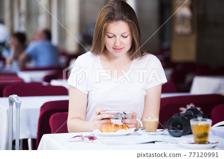 Tourist using mobile phone in cafe 77120991