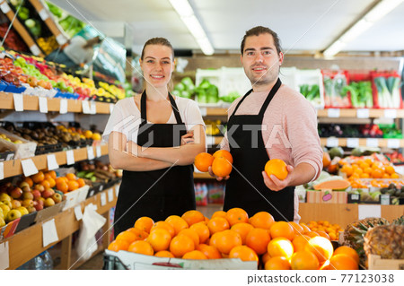 Young man and woman wearing aprons holding fresh oranges 77123038