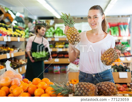 Young female holding fresh pineapples in fruit store Young female holding fresh pineapples in fruit store 77123059