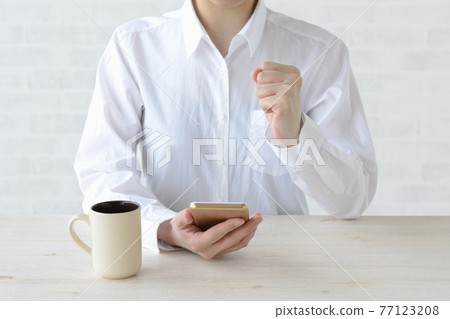 A woman who looks at a smartphone and plays a guts pose 77123208