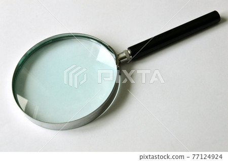 Magnifier with black handle on a white background. The handle is turned diagonally upwards. Magnifying transparent glass. View from above. Magnifier with black handle on a white background. The handle is turned diagonally upwards. Magnifying transparent glass. View from above. 77124924
