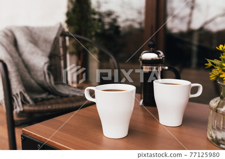 Two cups of coffee on the table on wooden brown terrace during evening sunset Two cups of coffee on the table on wooden brown terrace during evening sunset 77125980