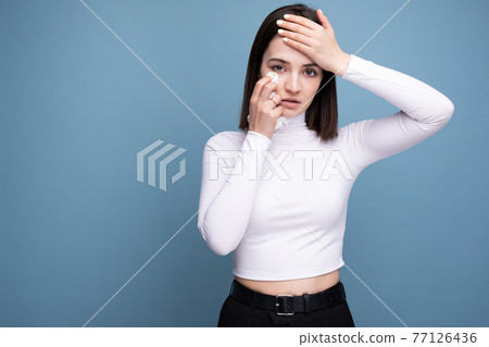 A woman with symptoms of a cold and headache holds in her hand in the studio on a blue background A woman with symptoms of a cold and headache holds in her hand in the studio on a blue background 77126436