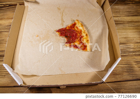 Bitten slice of pizza in cardboard box on a wooden table. Concept for home delivery of food, fast food, delivery of pizza 77126690