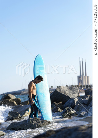 Surfer holding a surf board on beach Surfer holding a surf board on beach 77128319