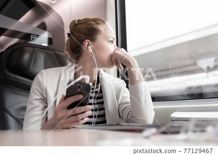 Businesswoman communicating on mobile phone while traveling by train. 77129467