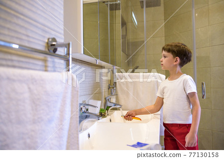A cute little boy is brushing his teeth with a toothbrush. On a pure white T-shirt in which he is dressed you can make an advertising inscription. The concept of children's health, medicine 77130158