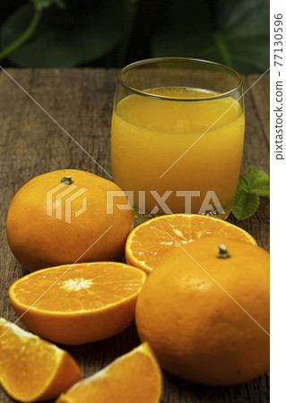 A glass of orange juice with orange fruit cut in half and orange slice on the wooden table. A glass of orange juice with orange fruit cut in half and orange slice on the wooden table. 77130596