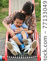 A 3-year-old boy playing with his grandma on a park slide 77133049