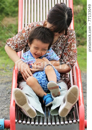 A 3-year-old boy playing with his grandma on a park slide 77133049