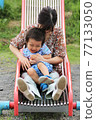 A 3-year-old boy playing with his grandma on a park slide 77133050