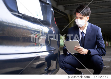 A man in a mask checking a car 77135347