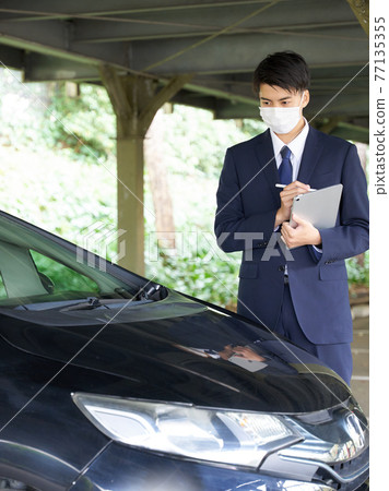A man in a mask checking a car 77135355