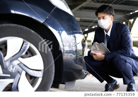 A man in a mask checking a car 77135359