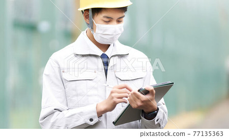 Men in work clothes wearing masks and using tablets 77135363