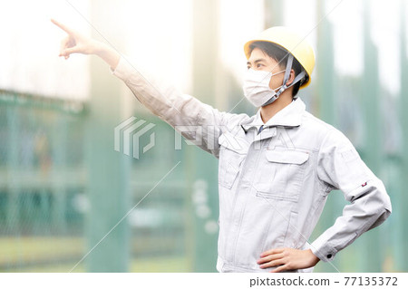 A man in work clothes wearing a mask and pointing his finger 77135372