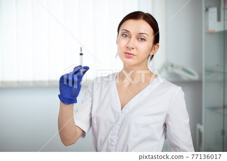 Portrait of confident professional female cosmetologist standing in modern medical esthetic office parlor, holding a syringe with beauty injection cocktail. Portrait of confident professional female cosmetologist standing in modern medical esthetic office parlor, holding a syringe with beauty injection cocktail. 77136017