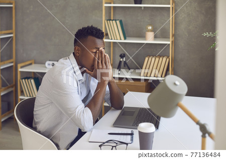 Black man sitting at his office desk feeling tired, overwhelmed and stressed out 77136484