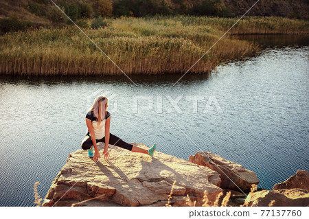 Young slim woman practicing yoga outdoors on stone shore of mountain river. Unity with nature concept Young slim woman practicing yoga outdoors on stone shore of mountain river. Unity with nature concept 77137760