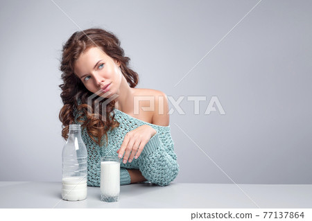 Beautiful young woman with glass of milk over grey background. 77137864