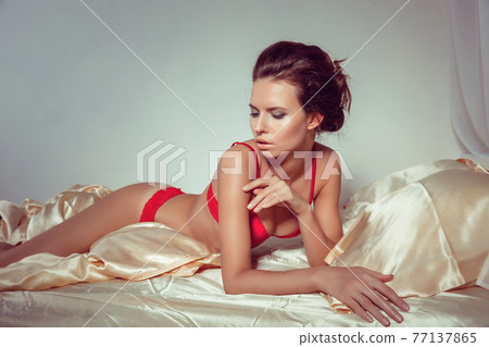 Attractive woman in sexy red lingerie lying in the seductive pose on bed Attractive woman in sexy red lingerie lying in the seductive pose on bed 77137865