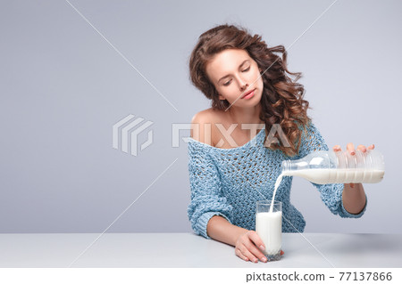 Beautiful woman pour out milk into glass Beautiful woman pour out milk into glass 77137866