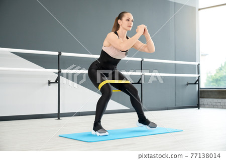 Muscular woman training legs using fitness band. 77138014