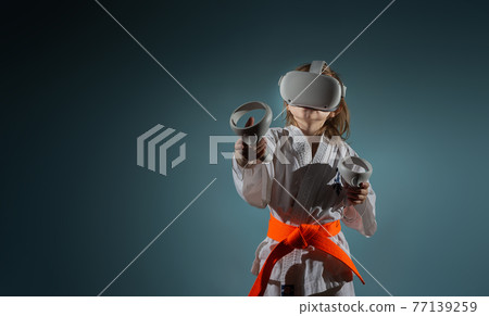 Caucasian little girl in karate uniform playing video games with VR headset 77139259