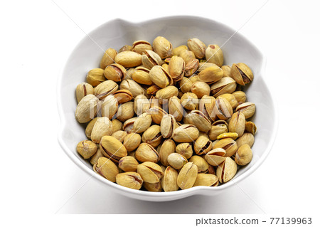 A white bowl with a bunch of salted and roasted pistachio seeds on a white background. Perfect shot for vegan diet,. 77139963