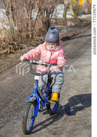 Little girl learns to ride a two-wheeled bicycle on the road in the village 77139974