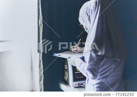 Muslim asian doctor with surgical mask analyzing blood sample of patient and take note. Muslim asian doctor with surgical mask analyzing blood sample of patient and take note. 77142250
