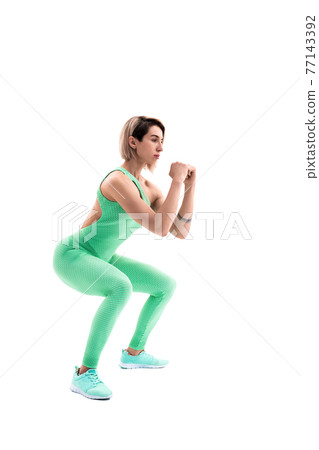Studio shot of an athletic woman doing squats isolated over whit Studio shot of an athletic woman doing squats isolated over whit 77143392