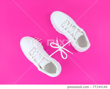 Pair of white sport shoes connected with laces bow on pink background. 77144140
