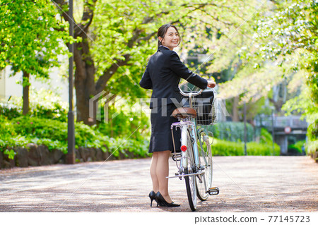 Young woman in a recruitment suit pulling a bicycle Young woman in a recruitment suit pulling a bicycle 77145723