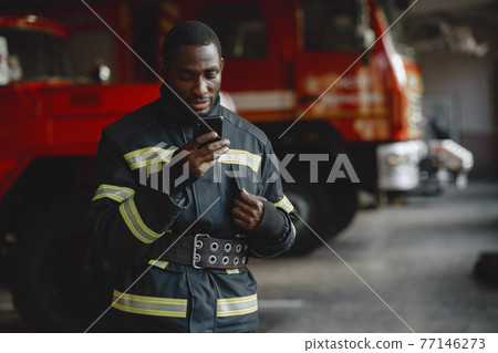 Portrait of a firefighter standing in front of a fire engine 77146273