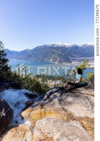Adventurous Adult Woman is sitting on top of a Beautiful Waterfall Adventurous Adult Woman is sitting on top of a Beautiful Waterfall 77146679