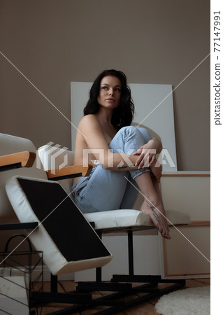 Relaxed topless woman sitting on chair at home 77147991