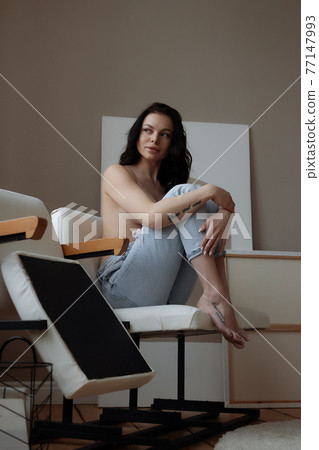 Relaxed topless woman sitting on chair at home Relaxed topless woman sitting on chair at home 77147993