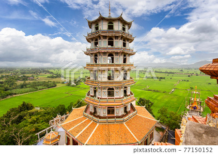 Aerial view of octagon pagoda at Wat Tham Khao Noi with the bright green rice field and blue sky in the background, Kanchanaburi 77150152
