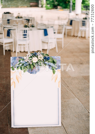 White blank board decorated with ornaments and flowers at the top stands at the entrance to the restaurant White blank board decorated with ornaments and flowers at the top stands at the entrance to the restaurant 77152600