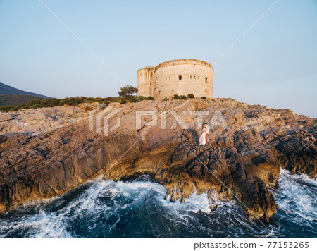 The bride and groom are embracing on the rocky seashore near the ancient fortress Arza The bride and groom are embracing on the rocky seashore near the ancient fortress Arza 77153265