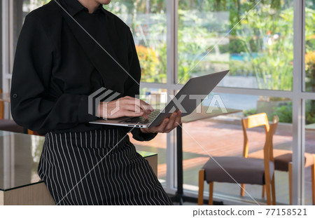 Barista in black apron using laptop while standing in cafe, coffee shop business. 77158521