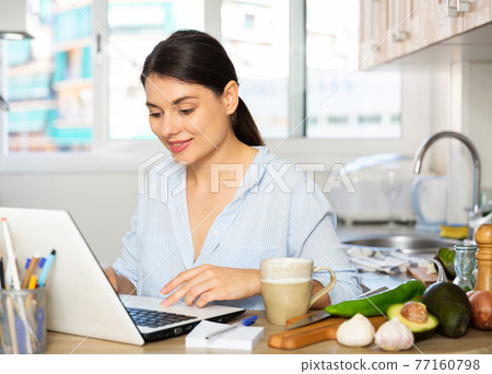 Woman sitting with laptop at kitchen 77160798