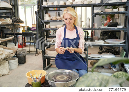 Creative moments. Portrait of happy woman in blue apron creating handmade clay ceramics in pottery workshop studio Creative moments. Portrait of happy woman in blue apron creating handmade clay ceramics in pottery workshop studio 77164779
