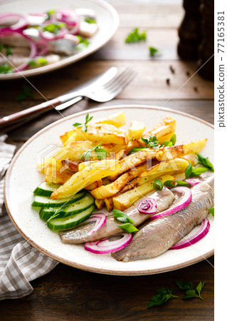 Pickled herring fillet with onion and fried potato on plate 77165381