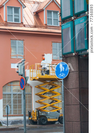 Painter with roller painting house facade in town 77168893