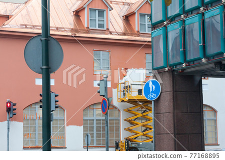 Painter with roller painting house facade in town Painter with roller painting house facade in town 77168895